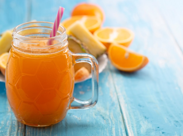 Der Glasbehälter mit dem Saft der Orange mit einem Strohhalm auf einer blauen Tabelle