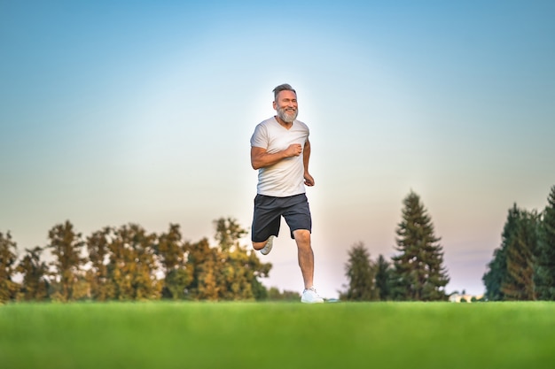 Der glückliche alte Sportler, der auf dem Gras läuft