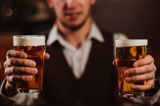 Der glückliche Barkeeper serviert zwei Gläser leichtes Bier vom Fass mit Schaum in der Hand an der Bar