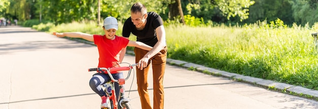 Der glückliche Familienvater bringt seiner Tochter bei, im Park in der Natur Fahrrad zu fahren.