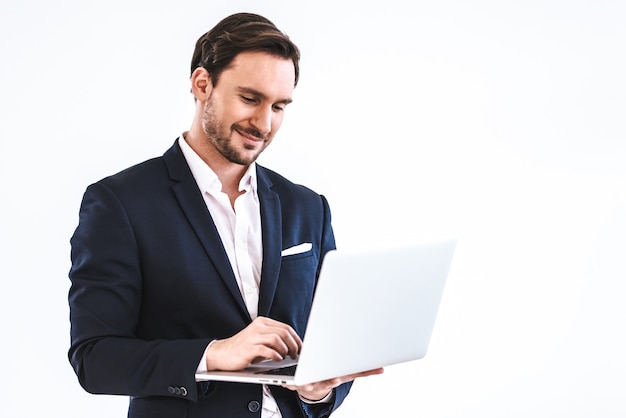 Der glückliche Geschäftsmann mit einem Laptop, der auf dem weißen Hintergrund steht