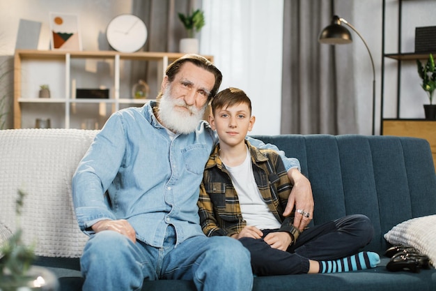 Der glückliche Großvater sitzt auf der Couch und verbringt gerne Zeit mit dem Enkel im schulpflichtigen Alter zu Hause