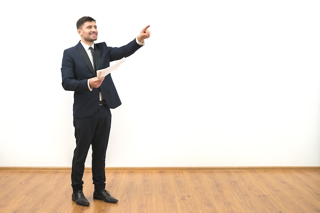 Der glückliche Mann mit Papieren, die auf den weißen Wandhintergrund gestikulieren