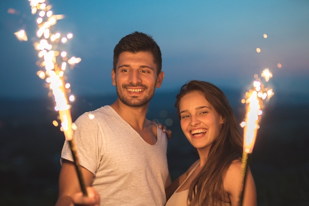 Der glückliche Mann und die Frau halten Feuerwerksstöcke. abend nacht zeit