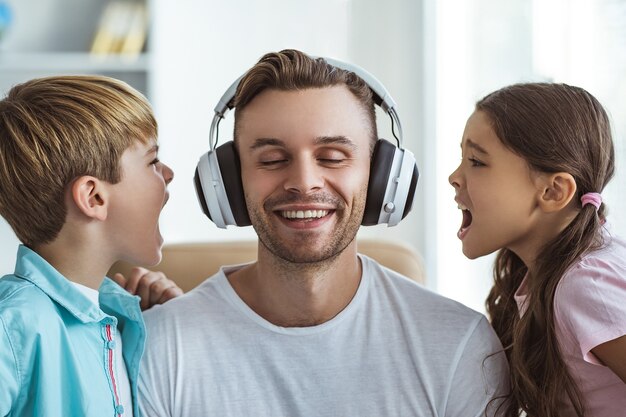 Der glückliche Vater mit Kopfhörern spielt mit einem Jungen und einem Mädchen am Tisch