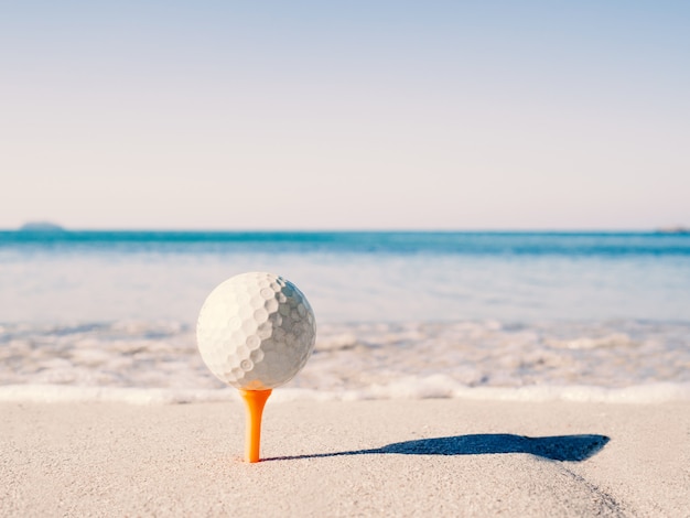 Der Golfball ist auf dem Abschlag, gestickt auf den Sandstrand mit dem Meer im Hintergrund.