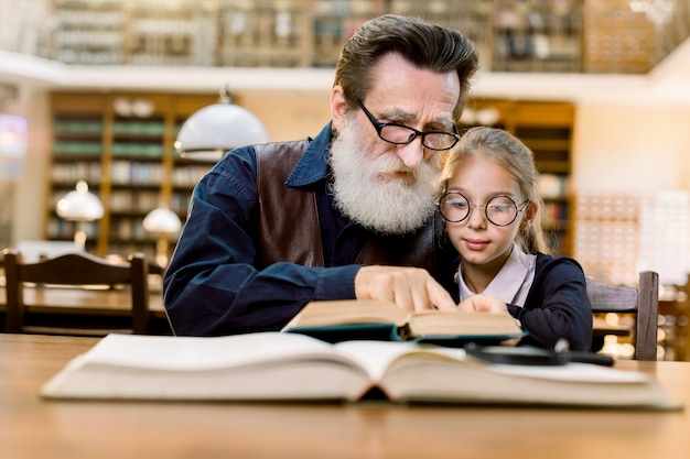 Der Großvater eines älteren Mannes und seine Enkelin lesen gemeinsam ein aufregendes Buch, während sie in der Bibliothek sitzen