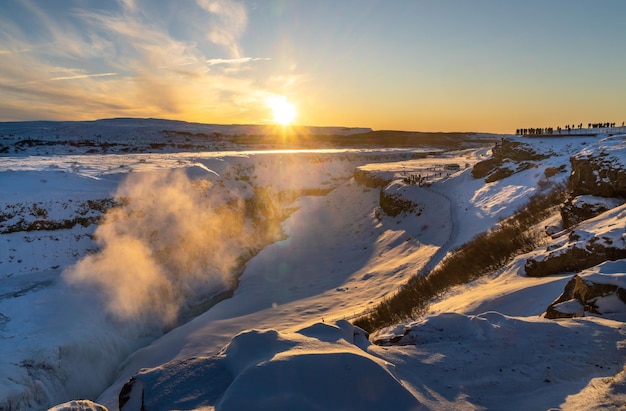 Der Gullfoss-Wasserfall durch die Dämmerungssonne, die den Nebel vom Fluss beleuchtet Silhouetten von Touristen