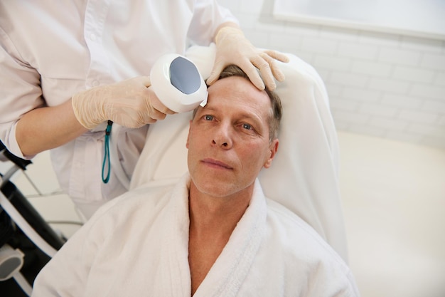 Der gutaussehende reife europäische Mann erhält im Wellnessbereich ein Verfahren zur Gesichtskonturierung mit Mesofäden zur Gesichtsverjüngung, Anti-Aging, Facelift und Mesotherapie. Männliches Kosmetikkonzept