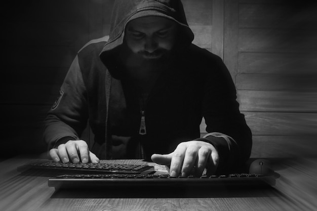 Der Hacker in der Haube sitzt und arbeitet hinter dem Computer