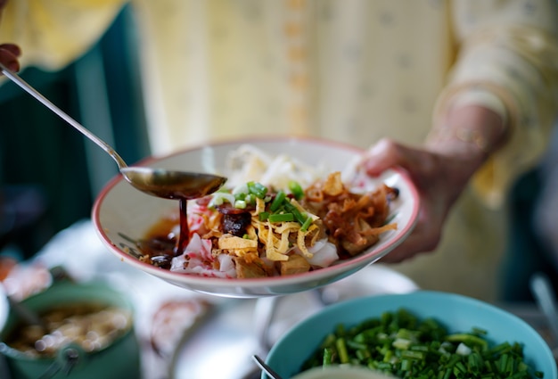 Der händler kocht sojasauce auf köstlichen chinesischen gedämpften reisnudelröllchen, die wunderschön in einem weißen teller angeordnet sind, um den kunden im lokalen restaurant zu bedienen.