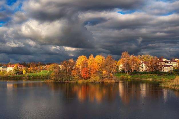 Der Himmel vor dem Sturm. Heller herbstlicher dramatischer Blick auf das Dorf am Ufer des Sees vor einem Gewitter.