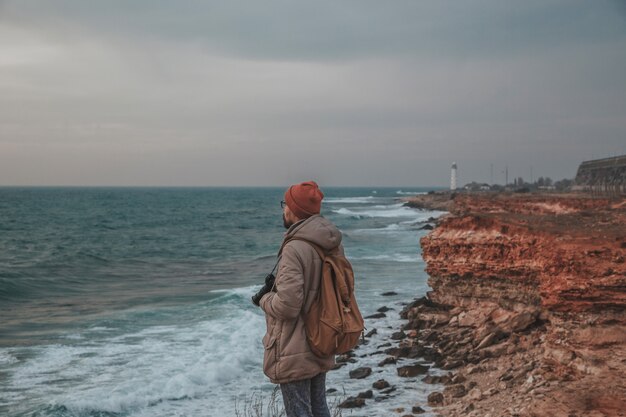 Der Hipster-Mann, der zum Leuchtturm am Meer schaut