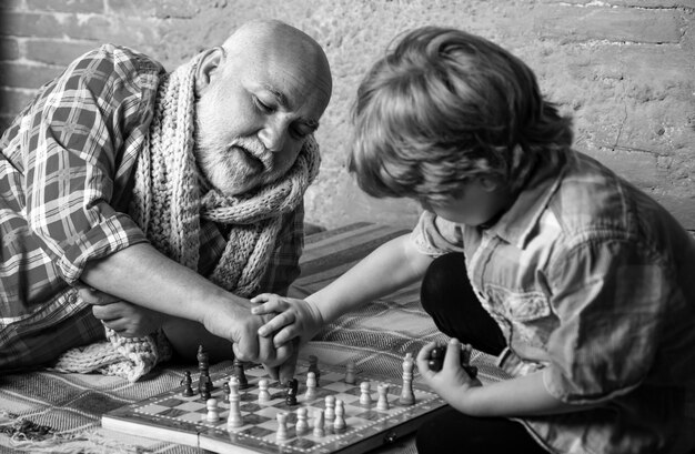 Foto der hübsche großvater und sein enkel spielen schach, während sie gemeinsam zu hause zeit verbringen.