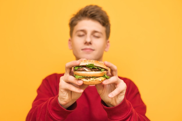 Der hübsche Kerl mit geschlossenen Augen zeigt der Kamera einen köstlichen großen Burger