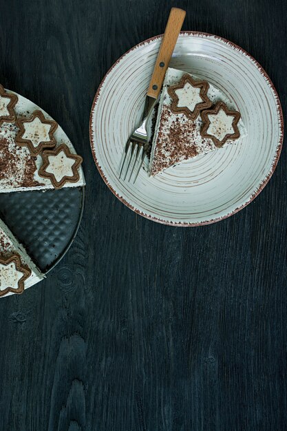 Der Hüttenkäsekuchen ist mit Keksen und geriebener schwarzer Schokolade auf dunklem Holz dekoriert