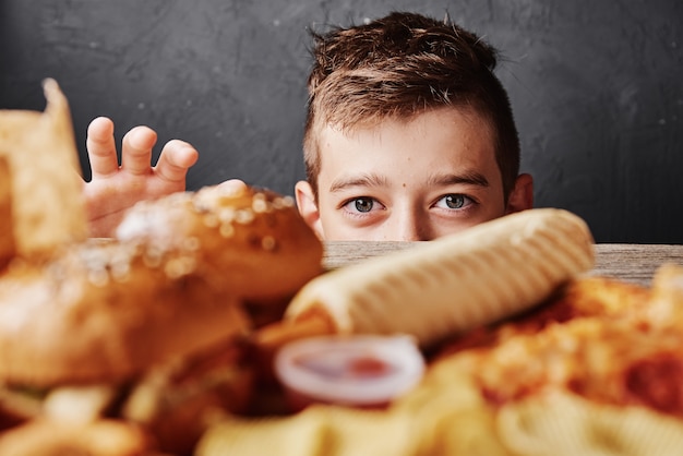 Der hungrige Junge schaut sich leckeres Essen an und nimmt den Hamburger vom Tisch.