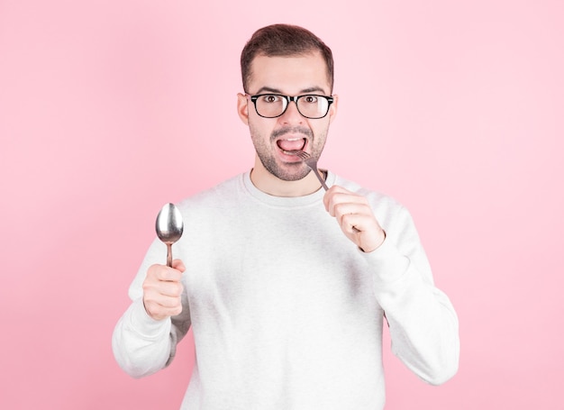 Der hungrige Mann leckt sich die Lippen, während er eine Gabel und einen Löffel in den Händen hält. Das Konzept von Ernährung, Nahrungsaufnahme und Hunger.