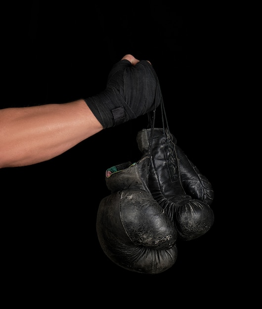 Der in einen schwarzen elastischen Sportverband gewickelte Arm hält zwei alte Vintage-Boxhandschuhe aus Leder