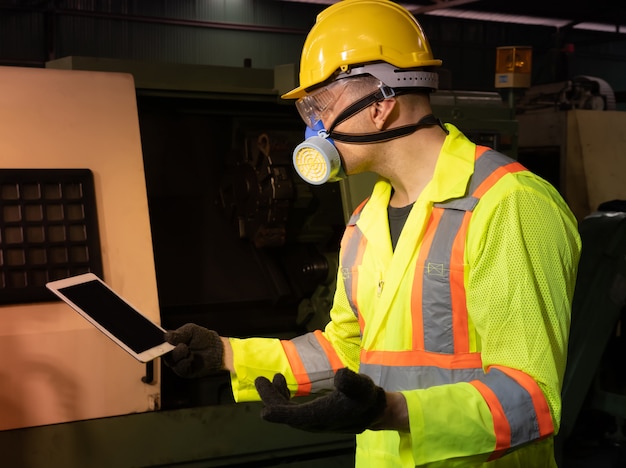 Der Ingenieur verwendet ein Computertablett mit einer Gasmaske im Gesicht und arbeitet in einer Industriefabrik.