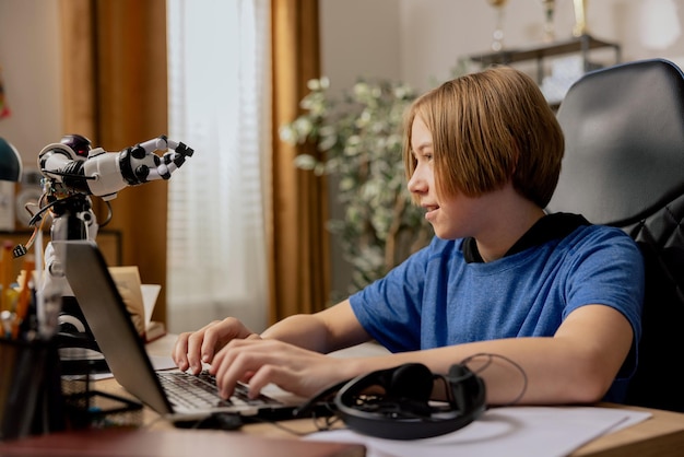 Der intelligente, lächelnde, ehrgeizige Junge sitzt am Schreibtisch vor dem Laptop und schaut sich den Roboter an, den er als Teenager testet