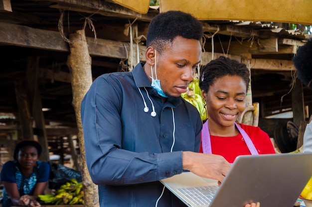 Der junge afrikanische Geschäftsmann ist aufgeregt, als er einer Marktfrau einige Informationen auf seinem Laptop zeigt.