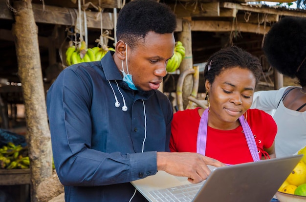 Der junge afrikanische Geschäftsmann ist aufgeregt, als er einer Marktfrau einige Informationen auf seinem Laptop zeigt.