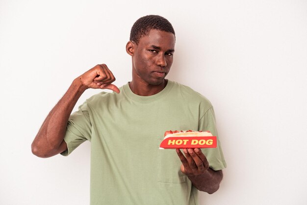 Der junge afroamerikanische Mann, der einen Hot Dog isst, der isoliert auf weißem Hintergrund ist, fühlt sich stolz und selbstbewusst, Beispiel zu folgen.