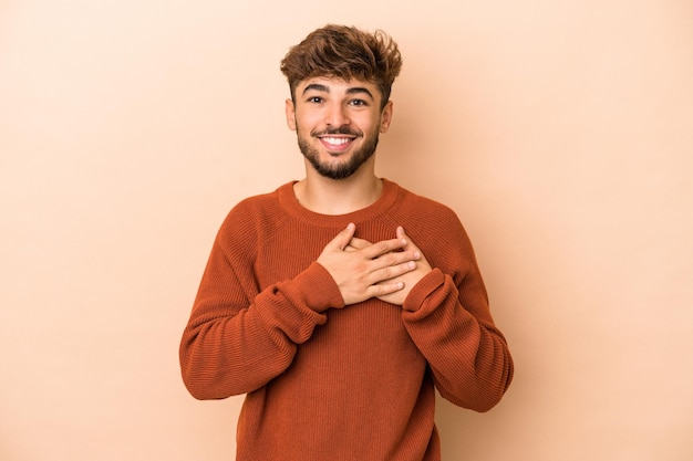 Der junge arabische mann, der auf beigem hintergrund isoliert ist, hat einen freundlichen ausdruck und drückt die handfläche an die brust. Liebe Konzept.