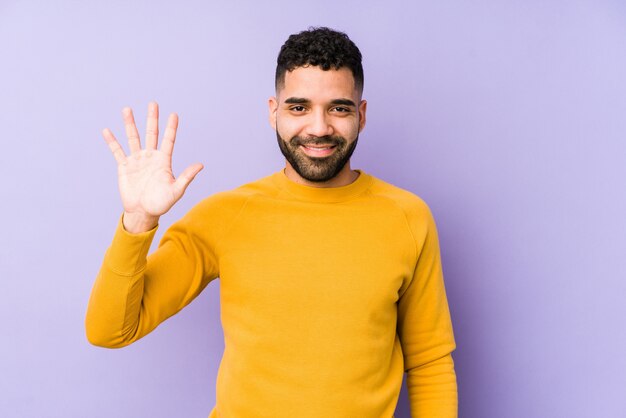 Der junge arabische Mann der gemischten Rasse isolierte lächelnd fröhlich und zeigte Nummer fünf mit den Fingern.