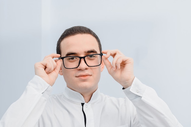 Der junge Arzt in einem medizinischen Gewand setzt eine Brille zum Sehen auf