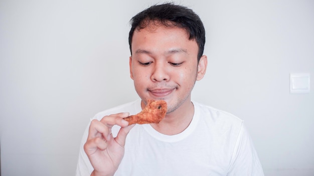 Der junge Asiate isst Brathähnchen und trägt ein weißes Hemd, das sich versucht und hungrig fühlt