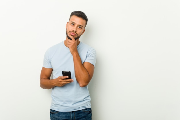 Der junge asiatische Mann der Mischrasse, der ein Telefon hält, entspannte sich das Denken an etwas