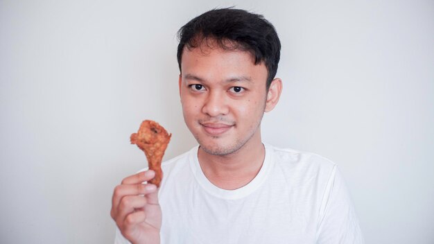 Der junge asiatische Mann isst gebratenes Hähnchen und trägt ein weißes Hemd, das sich glücklich fühlt und lächelt