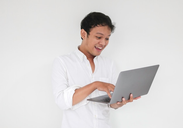 Der junge asiatische Mann lächelt und genießt es, wenn er zu Hause mit einem Laptop arbeitet. Konzept der Arbeit von zu Hause aus