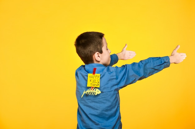 Der Junge auf gelbem Grund in einem blauen Hemd mit einem Klebeband und einem Stück Papier auf dem Rücken