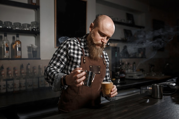 Der junge Barista in einer Schürze kocht Kaffee an der Bar in einem modernen Café