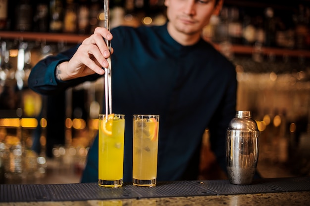 Der junge Barmann bereitet zwei alkoholische Cocktails zu und fügt Orangenstücke hinzu