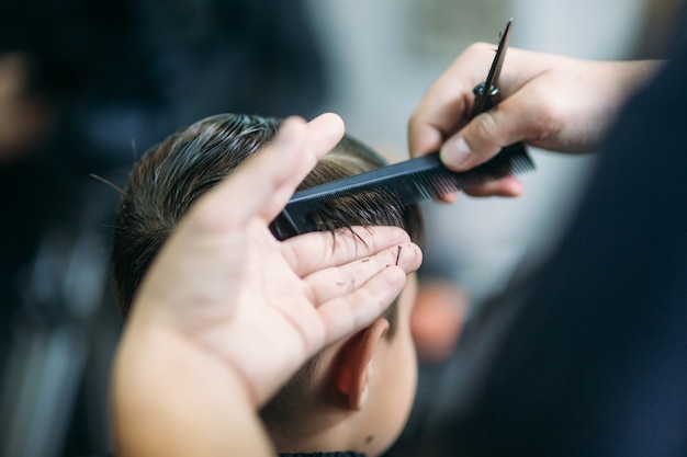 Der Junge bekommt Haarschnitt mit der Schere im Friseursalon