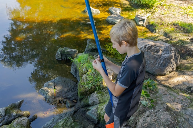Der Junge bereitet sich darauf vor, seine Stange zu werfen, nachdem er einen Haken und einen Köder vorbereitet hat. Sportfischerei im Sommer am Fluss