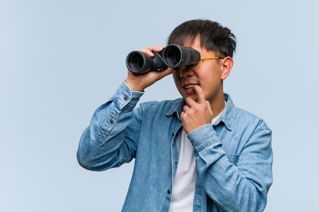 Der junge chinesische Mann, der Ferngläser hält, entspannte sich das Denken an etwas, das ein copyspace schaut