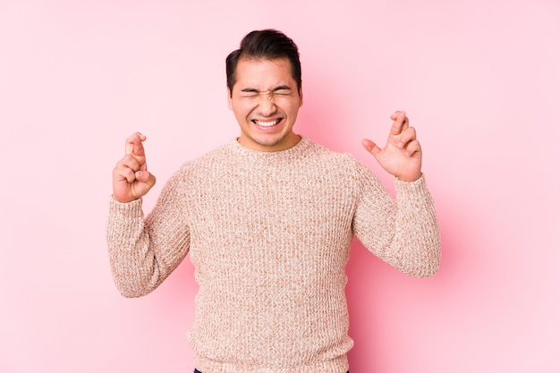 Der junge curvy Mann, der in einer rosa Wand aufwirft, lokalisierte Überfahrtfinger für das Haben des Glücks