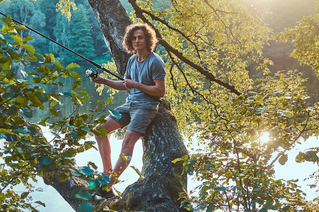 Der junge Fischer wartet auf große Fische, während er sich an die alte Birke in der Nähe des Sees lehnt. Es gibt schöne, sonnige Tage.