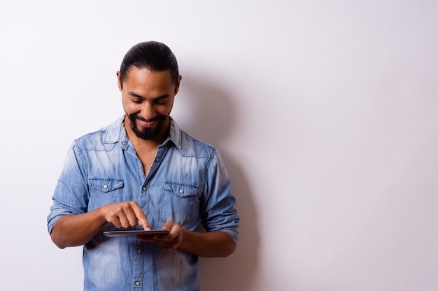 Der junge, gepflegte moderne Latino mit Bart lächelt zufrieden und zeigt mit dem Finger auf sein Tablet. Unternehmenskonzept.