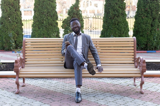 Der junge Geschäftsmann, der auf Stadtbank mit Telefon lächelt