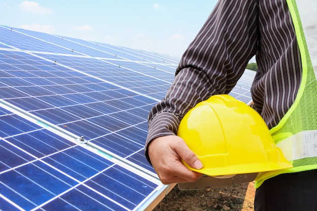 Der junge Geschäftsmanningenieur hält gelben Helm auf der Baustelle des Solarmodulkraftwerks