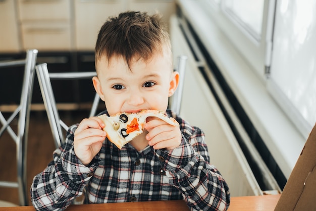 Der Junge in der Küche zu Hause isst Pizza mit Lachs