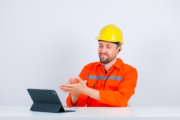 Der junge Ingenieur applaudiert, indem er vor seinem Tablet auf weißem Hintergrund sitzt