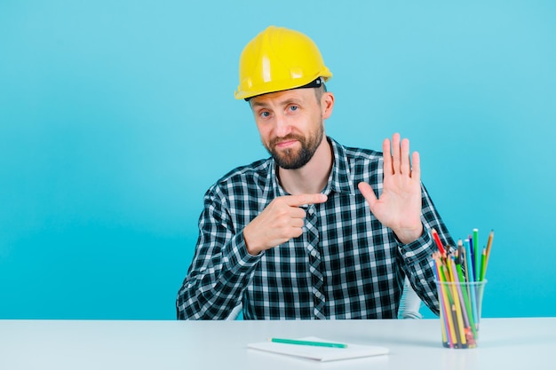 Der junge Ingenieur hebt seine Handvoll und zeigt sie mit dem Zeigefinger auf blauem Hintergrund