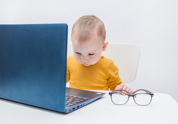 Der Junge ist mit einem Laptop beschäftigt. Fernunterricht. Einen Büroangestellten spielen. Ein Junge in einem gelben Body auf einem weißen Hintergrund. Augenprobleme, Augenkrankheiten, Myopie